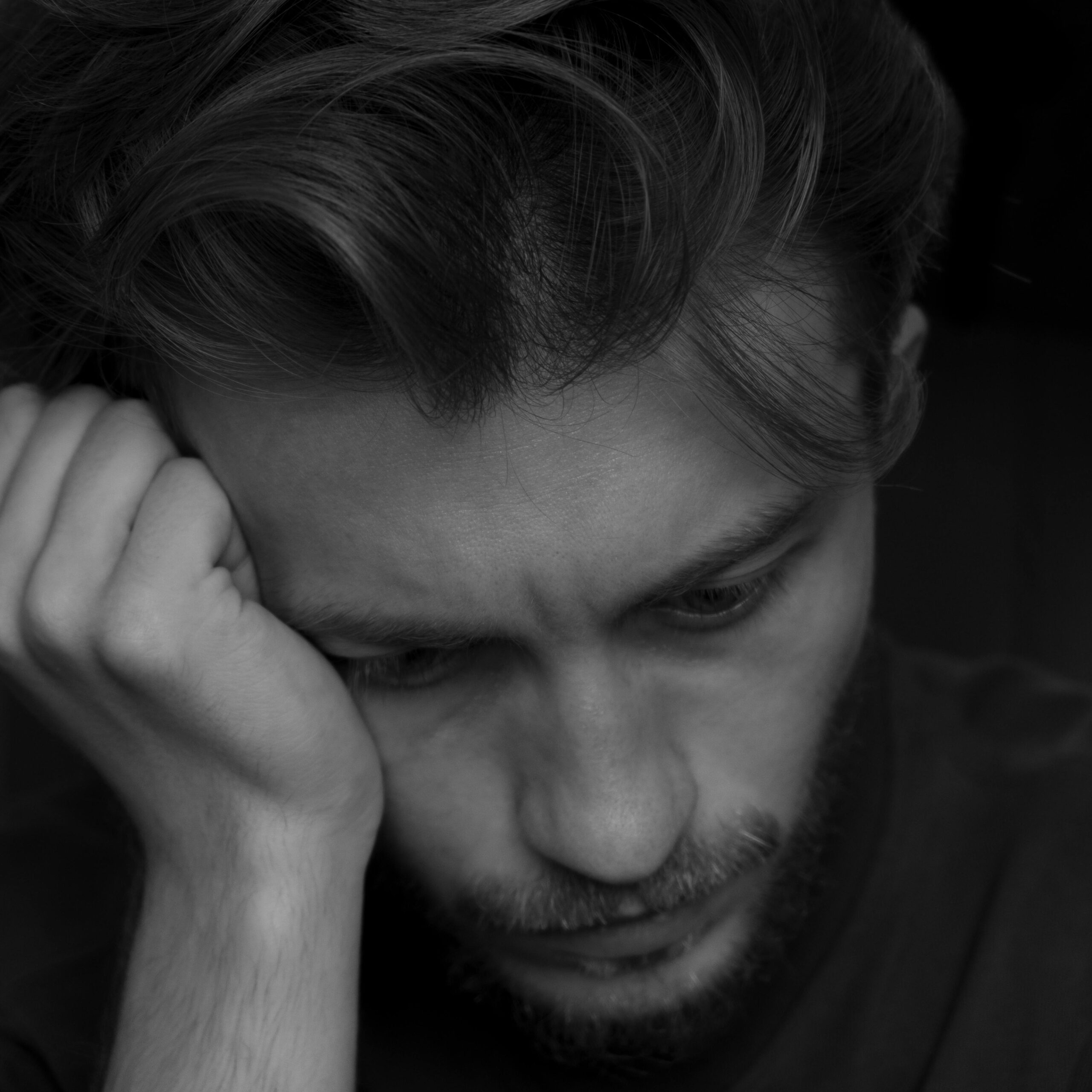 Close-up monochrome portrait of a pensive man looking down, conveying deep thoughts.